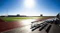 Deportes al aire libre scene, bright daylight, stadium bleachers and running track beside a green field.